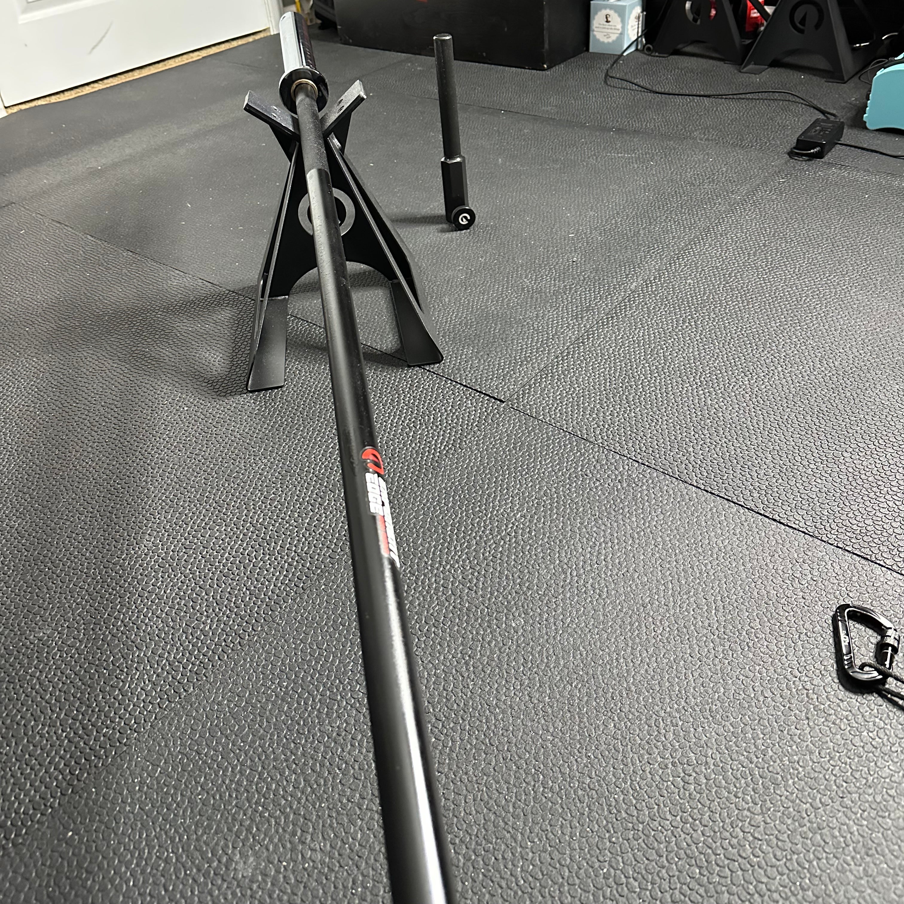 A black landmine bar with a knurled handle placed on a gray gym floor, with exercise equipment in the background.