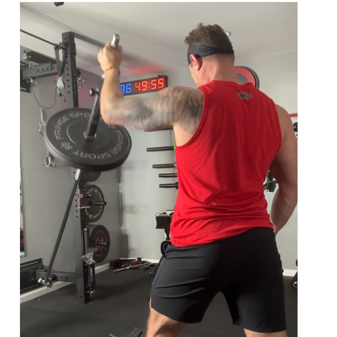 A person lifting a black landmine bar with a red shirt on in a gym setting.