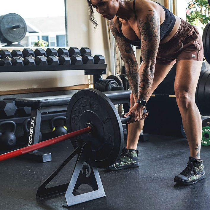 The Edge Landmine Jack is a compact landmine stand that takes the pain out of loading, reloading, and unloading heavy plates onto a barbell while using a landmine. This image presents a woman using the Edge Landmine Jack for a landmine workout.