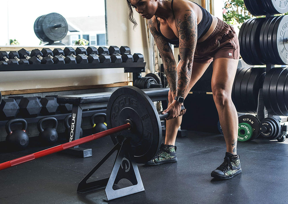 The Edge Landmine Jack is a compact landmine stand that takes the pain out of loading, reloading, and unloading heavy plates onto a barbell while using a landmine. This image presents a woman using the Edge Landmine Jack for a landmine workout.