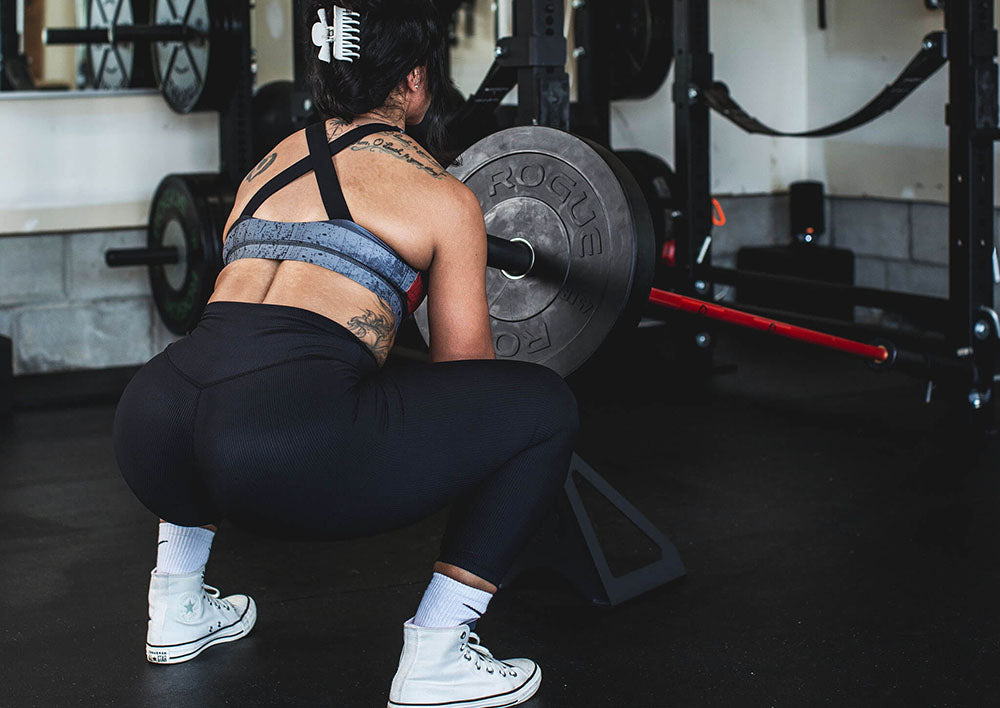 The Edge Landmine Jack is a compact landmine stand that takes the pain out of loading, reloading, and unloading heavy plates onto a barbell while using a landmine. This image presents a women using the Edge Landmine jack for a squat workout.