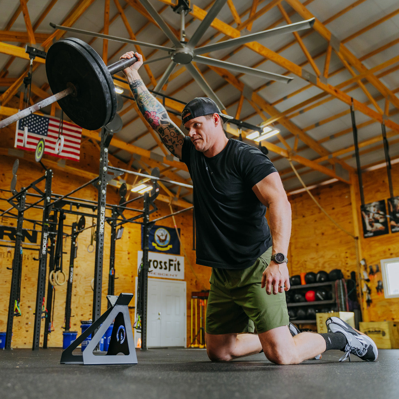 Man kneeling while lifting landmine bar with weights with landmine stand underneath