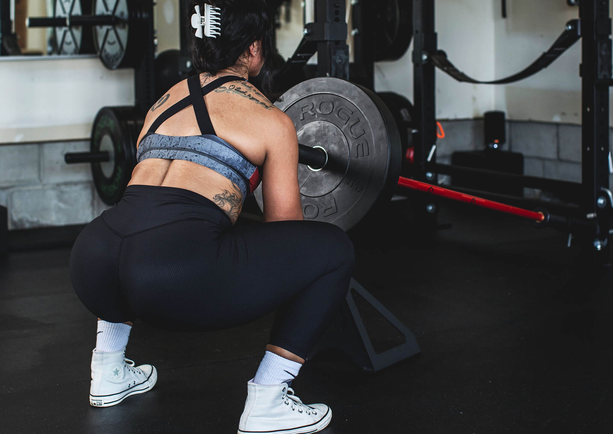 Woman performing deep landmine squat with a landmine jack underneath the barbell and weights in a home garage gym - The Landmine Jack by Exponent Edge