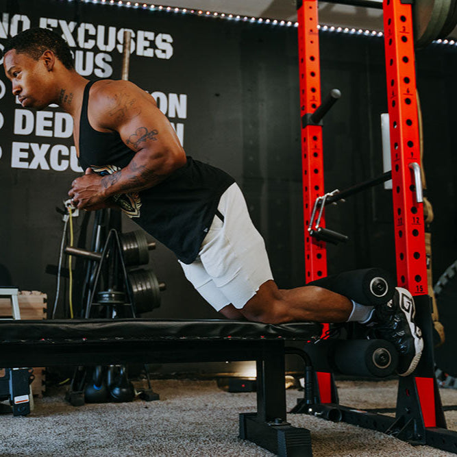 This Rack Mounted Glute Ham Developer is less bulky and lower priced than conventional GHDs. Perfect for glute workouts, ab workouts, and hamstring workouts. This image presents the Rack Mounted Glute Ham Developer being used by a man doing a hamstring workout.
