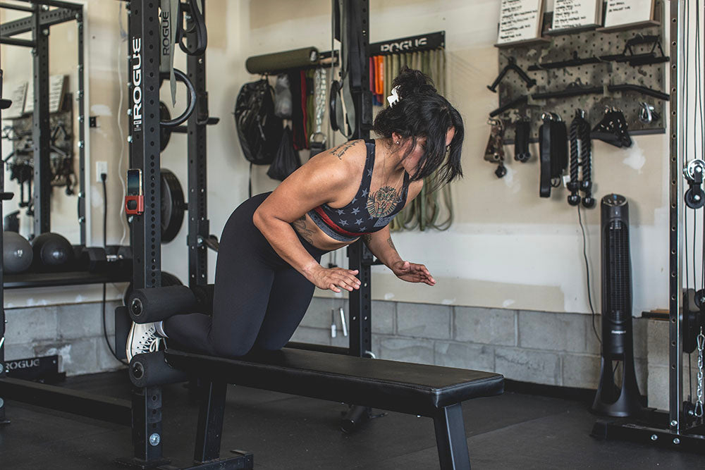 This Rack Mounted Glute Ham Developer is less bulky and lower priced than conventional GHDs. Perfect for glute workouts, ab workouts, and hamstring workouts. This image presents the Rack Mounted Glute Ham Developer being used by a woman for a hamstring workout in a home gym.